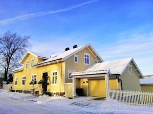 A yellow house surrounded by trees covered in the snow under a cloudy sky in Larvik in Norway